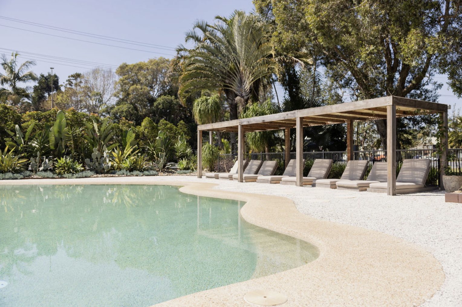 La piscina de arena y las reposeras bajo la pérgola, entre palmeras