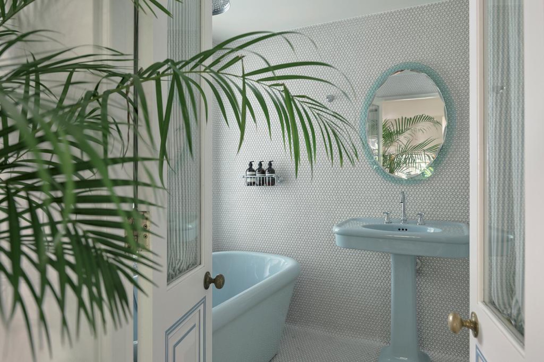 El baño con bañera, lavabo y espejo en celeste, y azulejo penny blanco