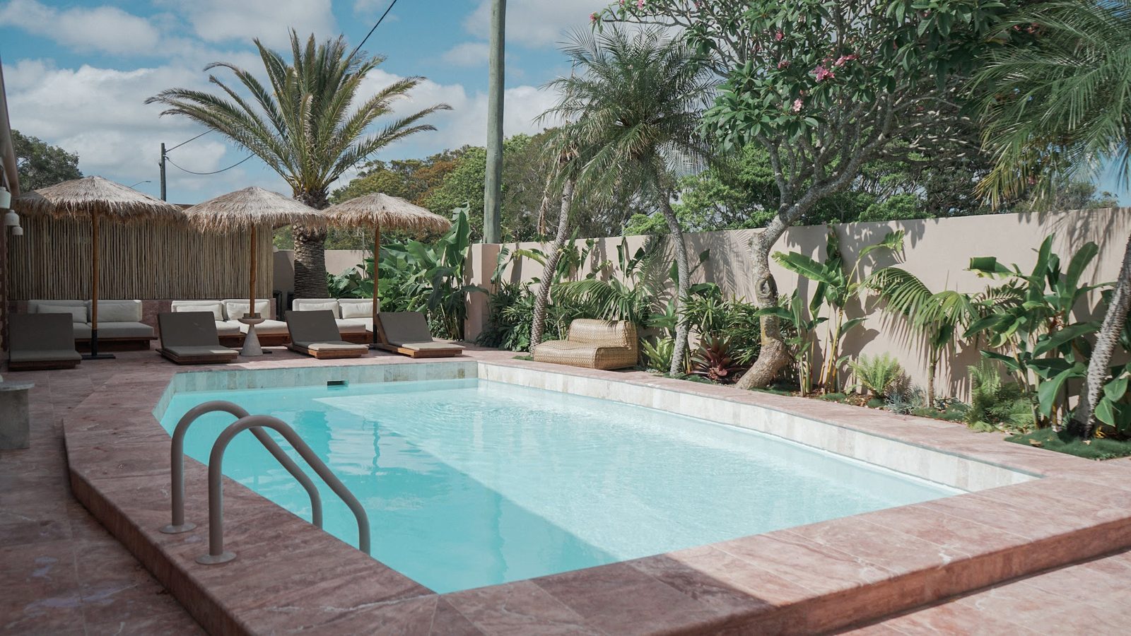 La piscina con reposeras y sombrillas de paja